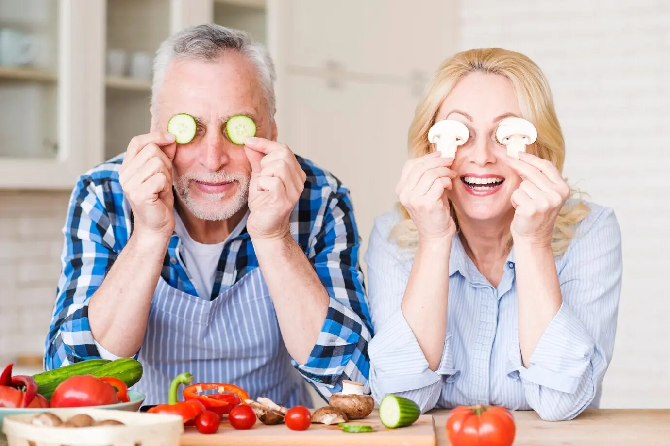 A portrait of an elderly couple covering their eyes with cucumber and mushroom slices.